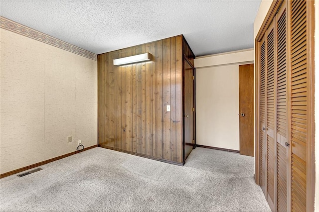 unfurnished bedroom with a textured ceiling, light carpet, and wooden walls