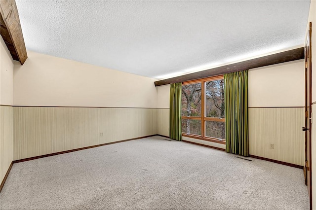 carpeted spare room featuring beamed ceiling, a textured ceiling, and wooden walls