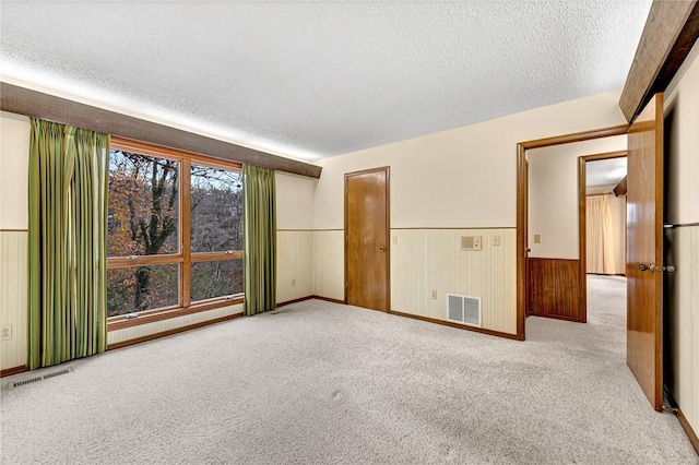 empty room with light carpet, a textured ceiling, and wooden walls