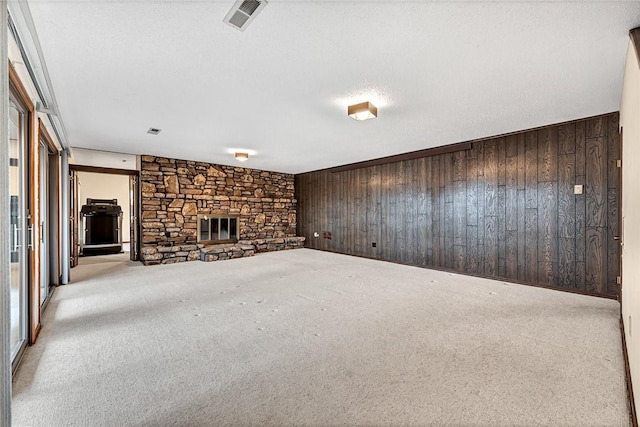 unfurnished living room with light carpet, a textured ceiling, a stone fireplace, and wooden walls