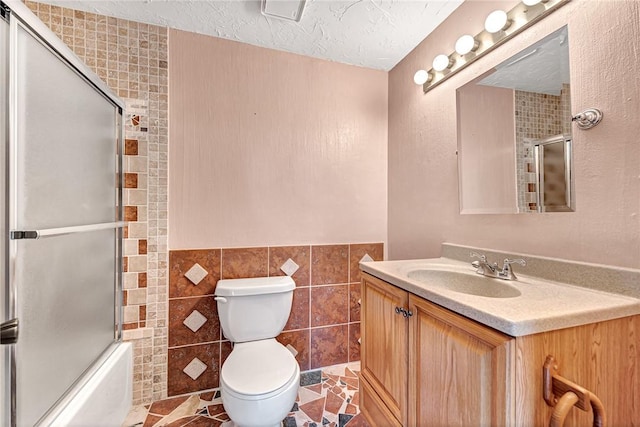 full bathroom with tile patterned flooring, combined bath / shower with glass door, toilet, vanity, and tile walls