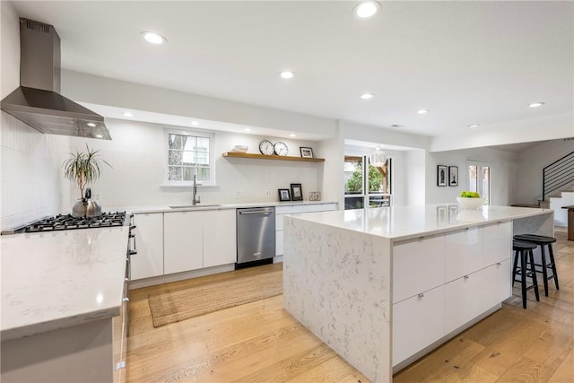 kitchen with white cabinets, plenty of natural light, a center island, and wall chimney range hood