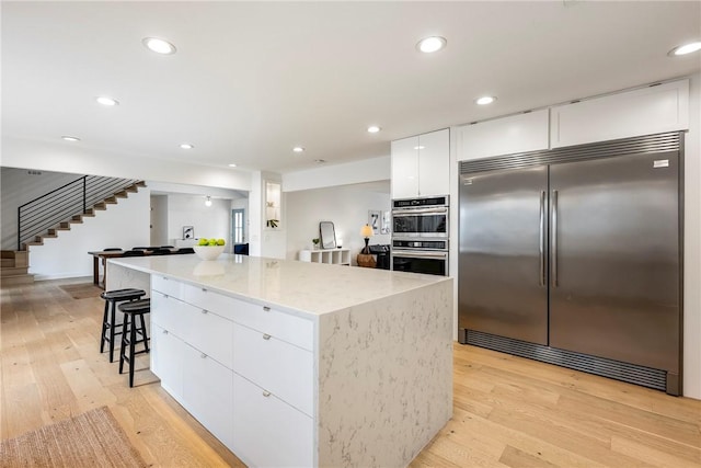 kitchen featuring white cabinets, appliances with stainless steel finishes, light hardwood / wood-style flooring, and a kitchen island