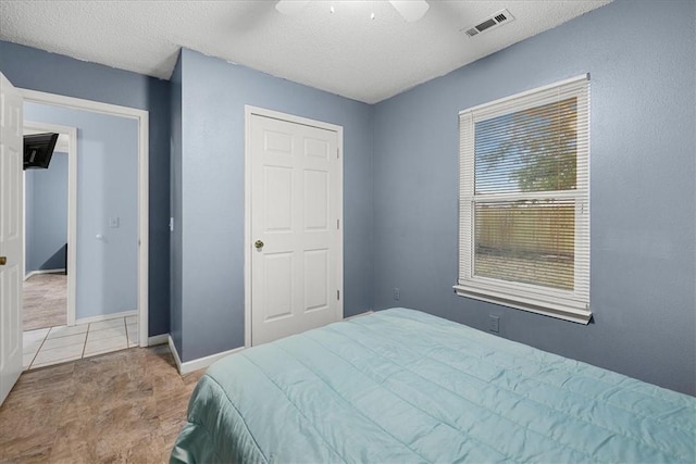 tiled bedroom with ceiling fan and a textured ceiling