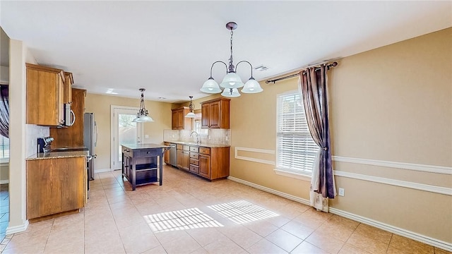 kitchen with brown cabinetry, decorative backsplash, a chandelier, a sink, and plenty of natural light