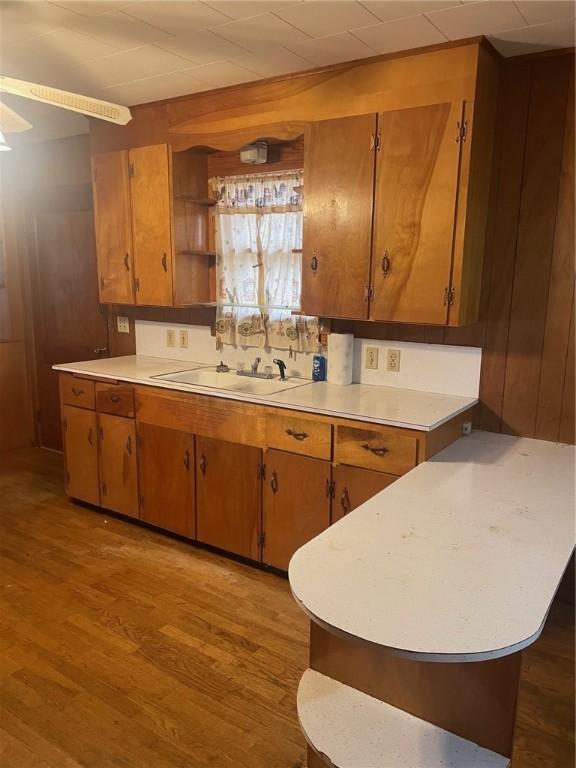 kitchen featuring ceiling fan, sink, tasteful backsplash, light hardwood / wood-style flooring, and wooden walls