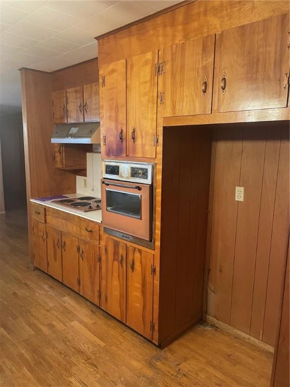 kitchen featuring white stovetop, light hardwood / wood-style flooring, oven, and wood walls