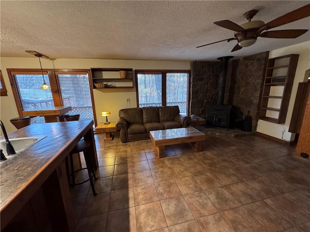 living room featuring a wood stove, ceiling fan, sink, a textured ceiling, and dark tile patterned flooring