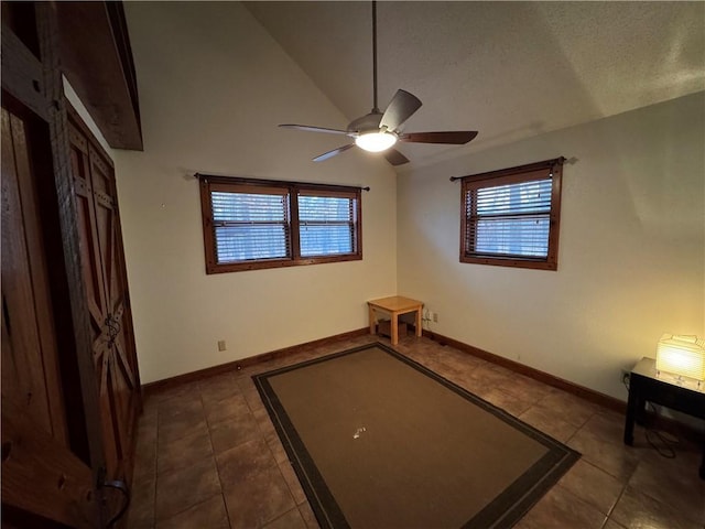 tiled empty room with a textured ceiling, lofted ceiling, ceiling fan, and a healthy amount of sunlight