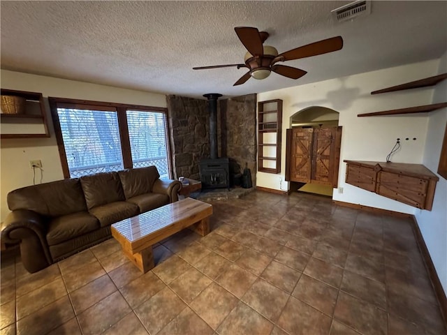 unfurnished living room featuring a textured ceiling, a wood stove, and ceiling fan