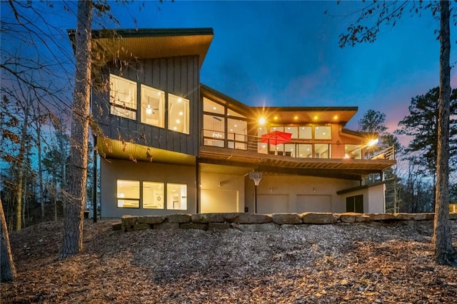 back house at dusk with a sunroom, a balcony, and a garage