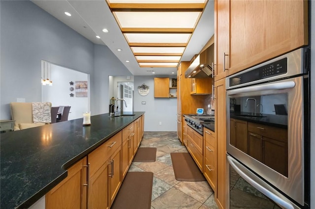 kitchen with dark stone counters, stainless steel appliances, wall chimney range hood, sink, and hanging light fixtures