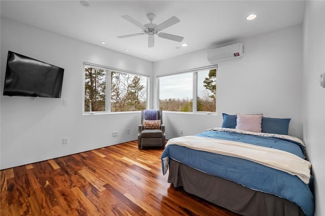 bedroom with a wall mounted AC, ceiling fan, and wood-type flooring