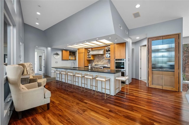 kitchen featuring backsplash, wall chimney range hood, high vaulted ceiling, dark hardwood / wood-style floors, and a breakfast bar area