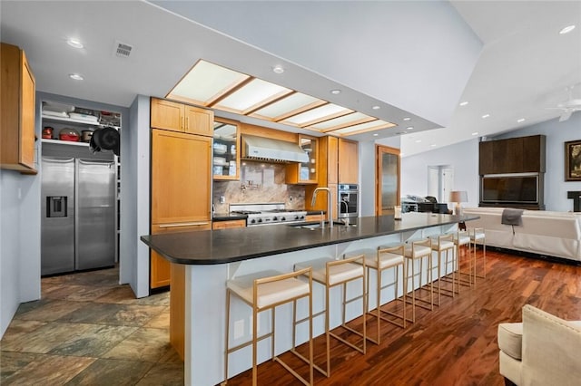 kitchen with stainless steel appliances, a kitchen island with sink, sink, a breakfast bar area, and range hood