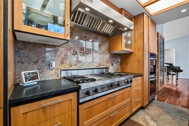 kitchen featuring appliances with stainless steel finishes, tasteful backsplash, a skylight, wall chimney range hood, and light hardwood / wood-style floors