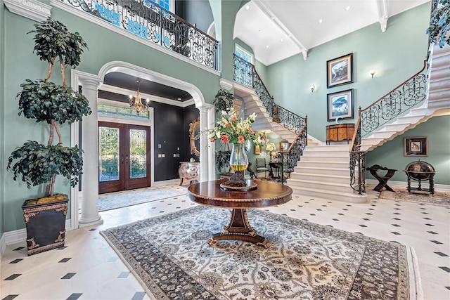 entryway with decorative columns, french doors, a high ceiling, and ornamental molding