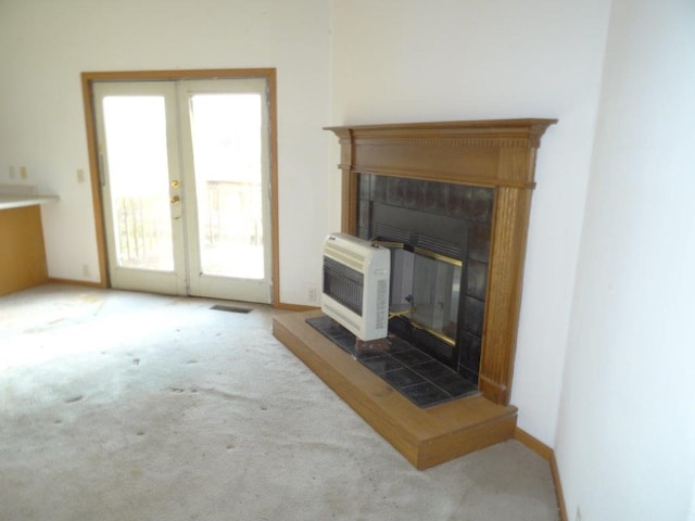 carpeted living room with heating unit, a wealth of natural light, french doors, and a fireplace