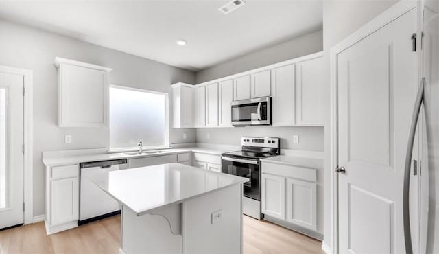 kitchen featuring stainless steel appliances, a kitchen island, white cabinetry, and light hardwood / wood-style flooring