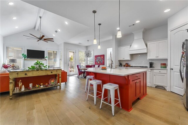 kitchen with a kitchen bar, decorative backsplash, premium range hood, a kitchen island with sink, and light hardwood / wood-style floors