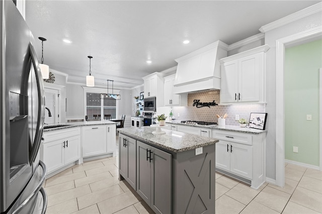 kitchen featuring light stone countertops, appliances with stainless steel finishes, custom exhaust hood, white cabinets, and a kitchen island