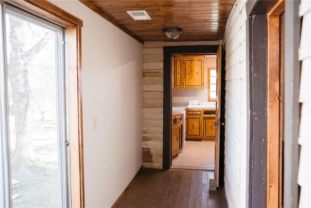 hall with light wood-type flooring, wooden ceiling, and wood walls