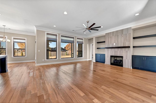 unfurnished living room with a large fireplace, built in features, crown molding, light hardwood / wood-style floors, and ceiling fan with notable chandelier