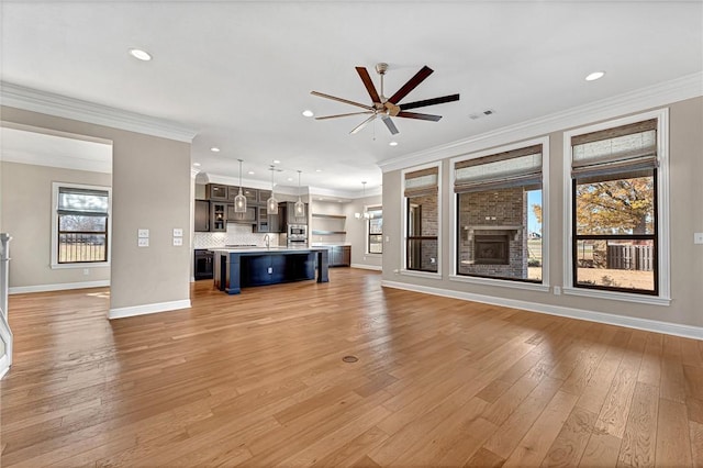 unfurnished living room featuring ceiling fan, light wood-type flooring, ornamental molding, and a brick fireplace