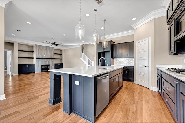 kitchen with a kitchen island with sink, hanging light fixtures, sink, appliances with stainless steel finishes, and light hardwood / wood-style floors