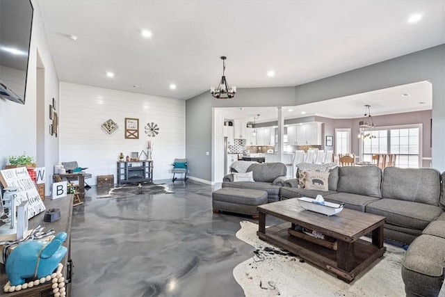 living room with a chandelier, concrete floors, and wood walls