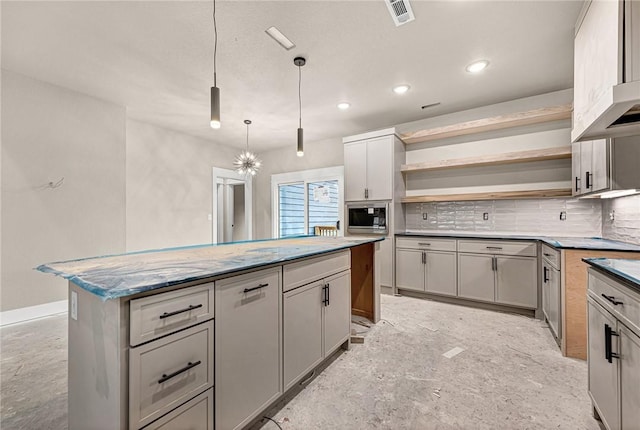 kitchen with stainless steel microwave, gray cabinetry, decorative backsplash, hanging light fixtures, and a center island