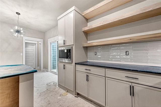 kitchen featuring pendant lighting, an inviting chandelier, backsplash, stainless steel microwave, and white cabinets