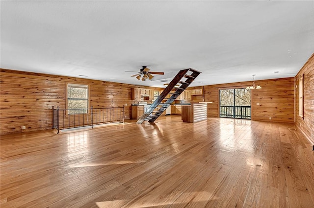 unfurnished living room with wooden walls, light hardwood / wood-style floors, and ceiling fan with notable chandelier