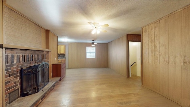 living room featuring a brick fireplace, ceiling fan, wood walls, and light hardwood / wood-style flooring