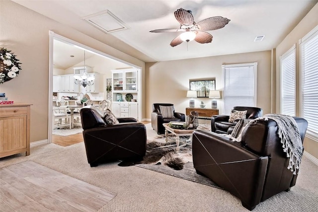 living area with ceiling fan with notable chandelier, carpet floors, vaulted ceiling, and baseboards