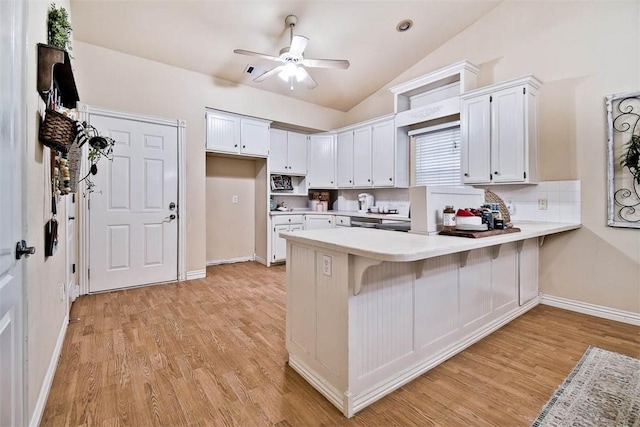 kitchen featuring a peninsula, white cabinetry, vaulted ceiling, light countertops, and light wood finished floors