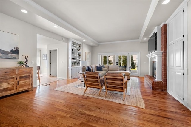 living room featuring light wood-type flooring, a brick fireplace, and crown molding