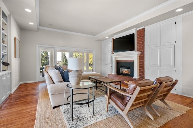 living room featuring crown molding, light hardwood / wood-style floors, and a brick fireplace