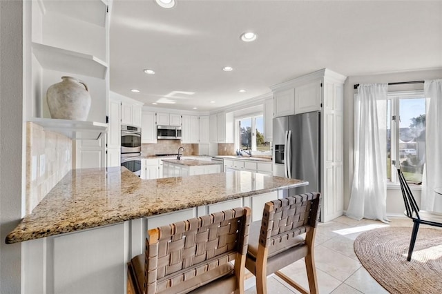 kitchen with light stone countertops, stainless steel appliances, light tile patterned floors, tasteful backsplash, and white cabinets