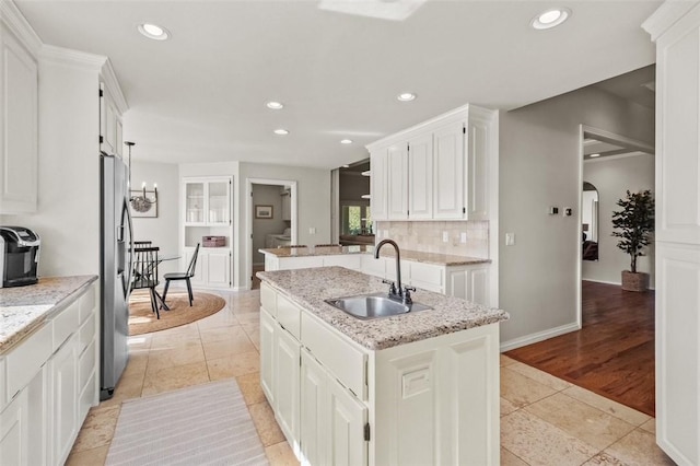 kitchen featuring white cabinetry, sink, stainless steel refrigerator with ice dispenser, light hardwood / wood-style floors, and a kitchen island with sink