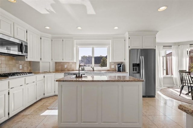 kitchen with white cabinets, decorative backsplash, an island with sink, and appliances with stainless steel finishes