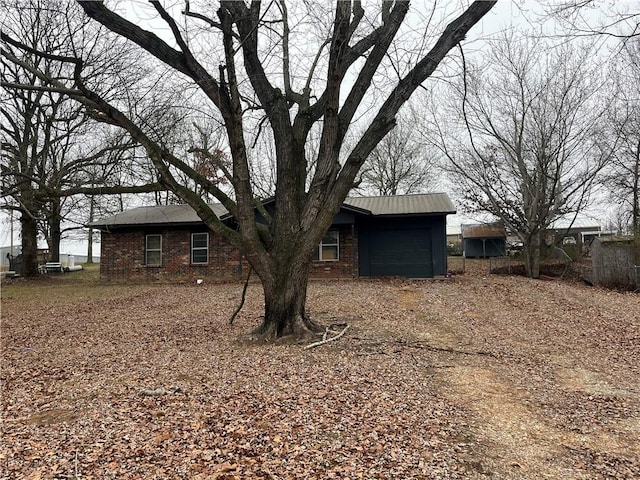 exterior space featuring metal roof, driveway, brick siding, and an attached garage