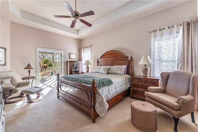 carpeted bedroom with ceiling fan, access to exterior, and a tray ceiling