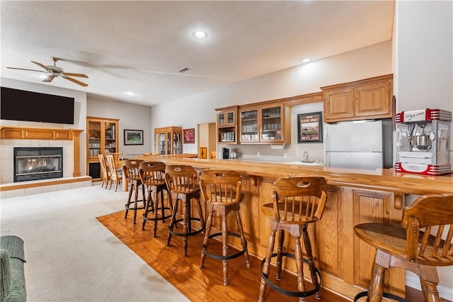 kitchen featuring a kitchen bar, sink, carpet floors, white fridge, and a tiled fireplace