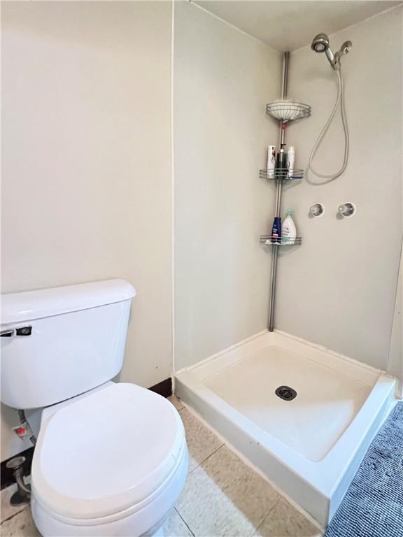 bathroom with tile patterned floors, toilet, and a shower