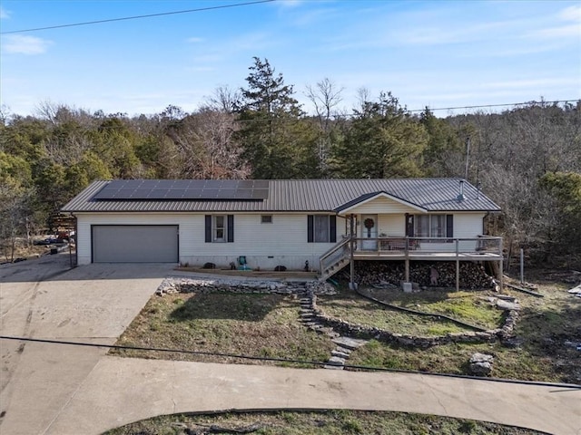 single story home with a garage, driveway, solar panels, metal roof, and a wooded view