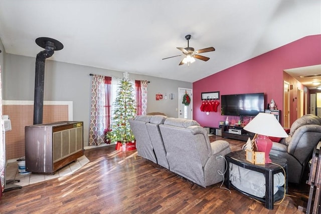 living area featuring ceiling fan, vaulted ceiling, wood finished floors, and a wood stove