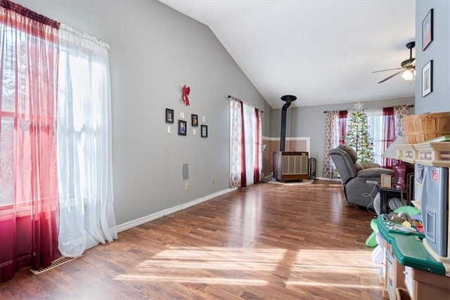 office with lofted ceiling, ceiling fan, wood finished floors, visible vents, and a wood stove