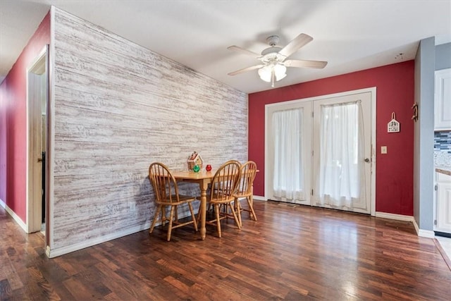 dining room with ceiling fan, an accent wall, baseboards, and wood finished floors