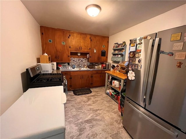 kitchen featuring range with gas stovetop, sink, stainless steel refrigerator, and tasteful backsplash